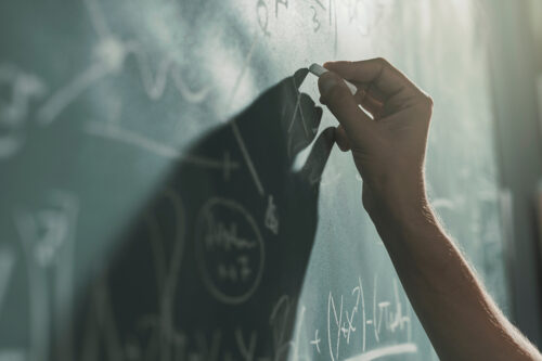 Professor writing mathematical formulas on the chalkboard, hand close up