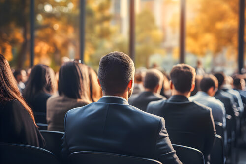 Business people sitting as an audience at a business convention or event in a meeting room listening to a lecture. Back view and blurred background with copy space
